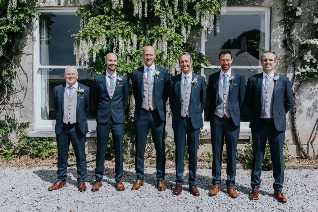 Groom and groomsmen outside Burncoose House with wisteria